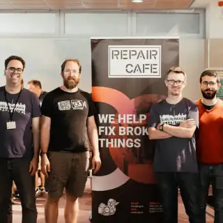 Group of people smiling in front of a Repair Cafe banner